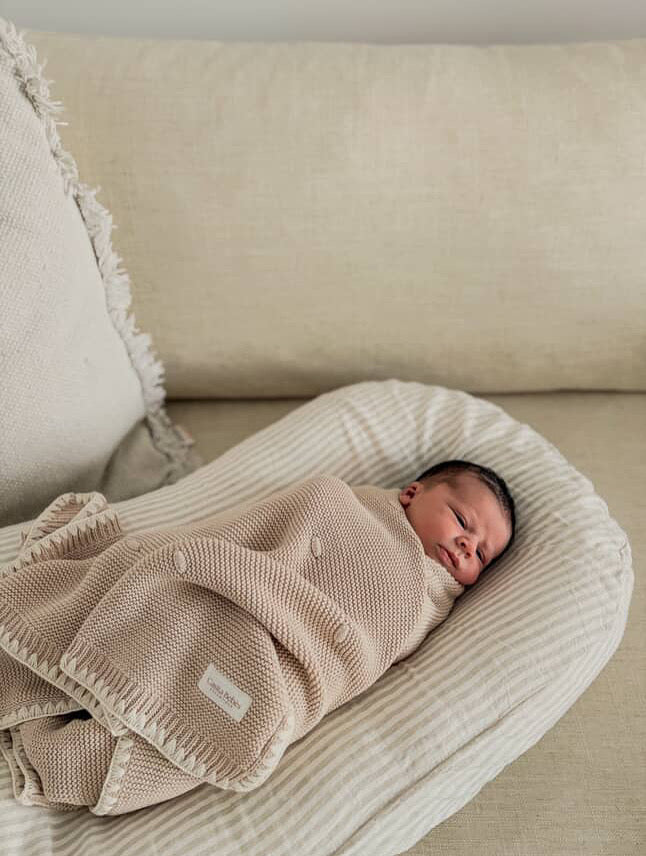 Newborn baby swaddled in a brow blanket on a soft surface with casita Bebes brand