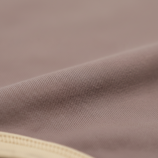 Close-up of soft mauve organic cotton fabric from Mamīta Alaina bodysuit with cream trim detailing.