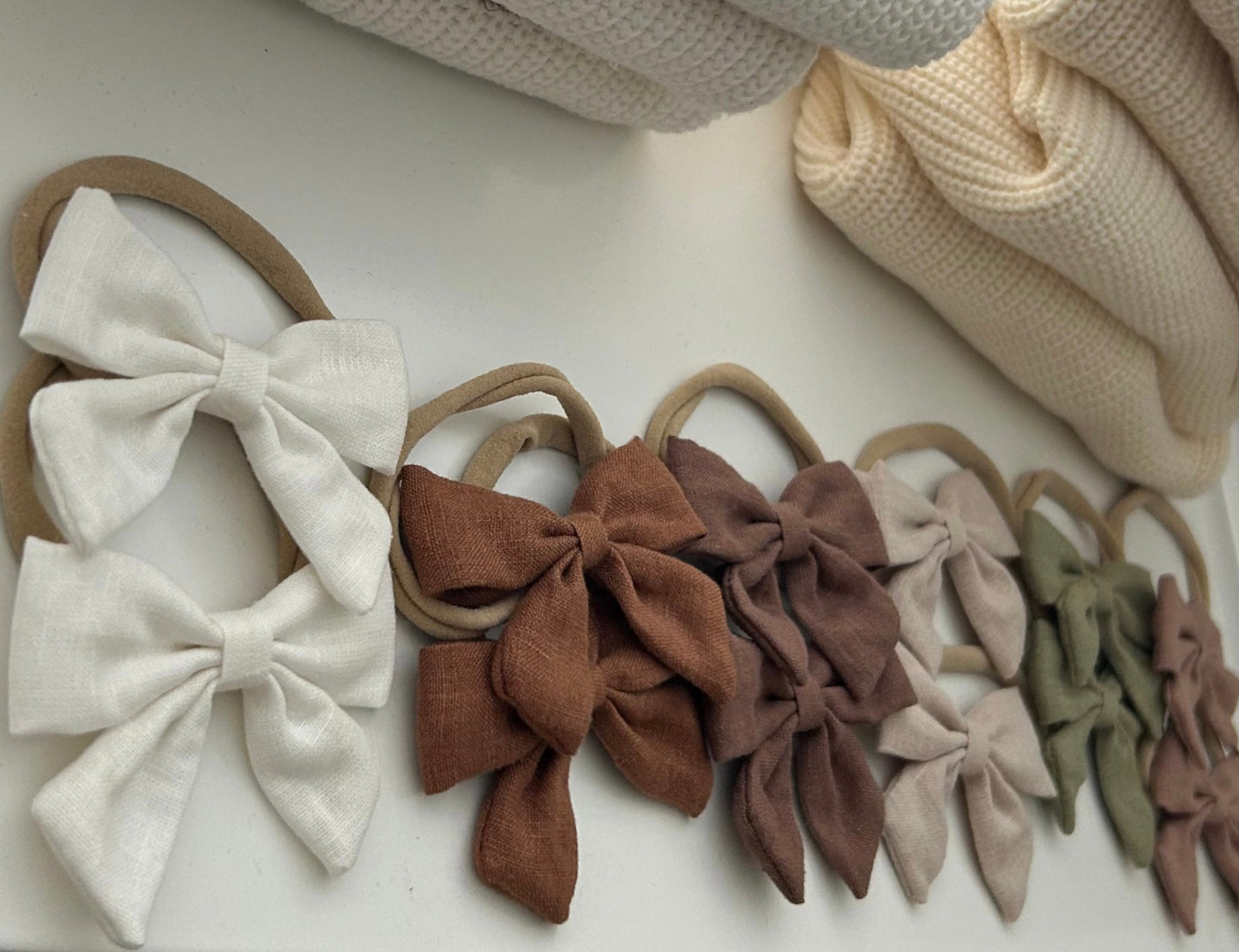 Set of fabric hair bows in various colors on a white surface with textured fabric in the background.