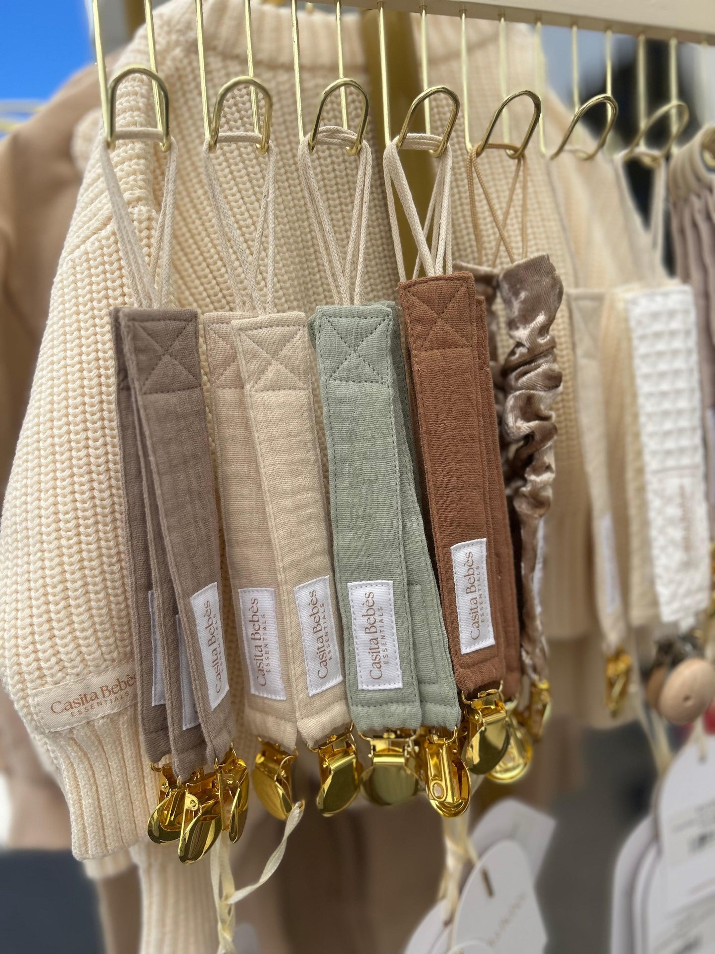 Set of organic certified Essentīals Gold Dummy Holders in dusty beige, green, brown, and khaki with gold clips, displayed on .