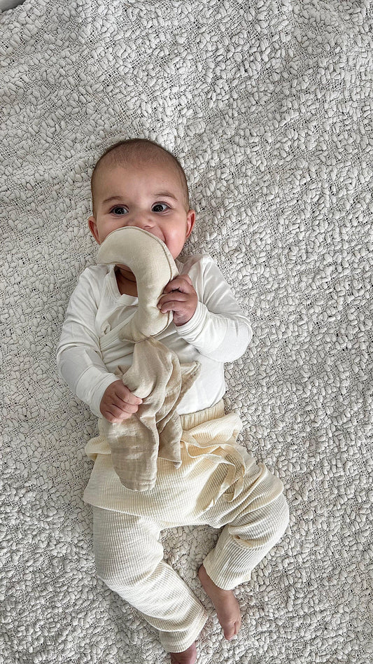 Baby wearing organic cotton Essentīals Cuddly Moon comforter on textured white blanket.