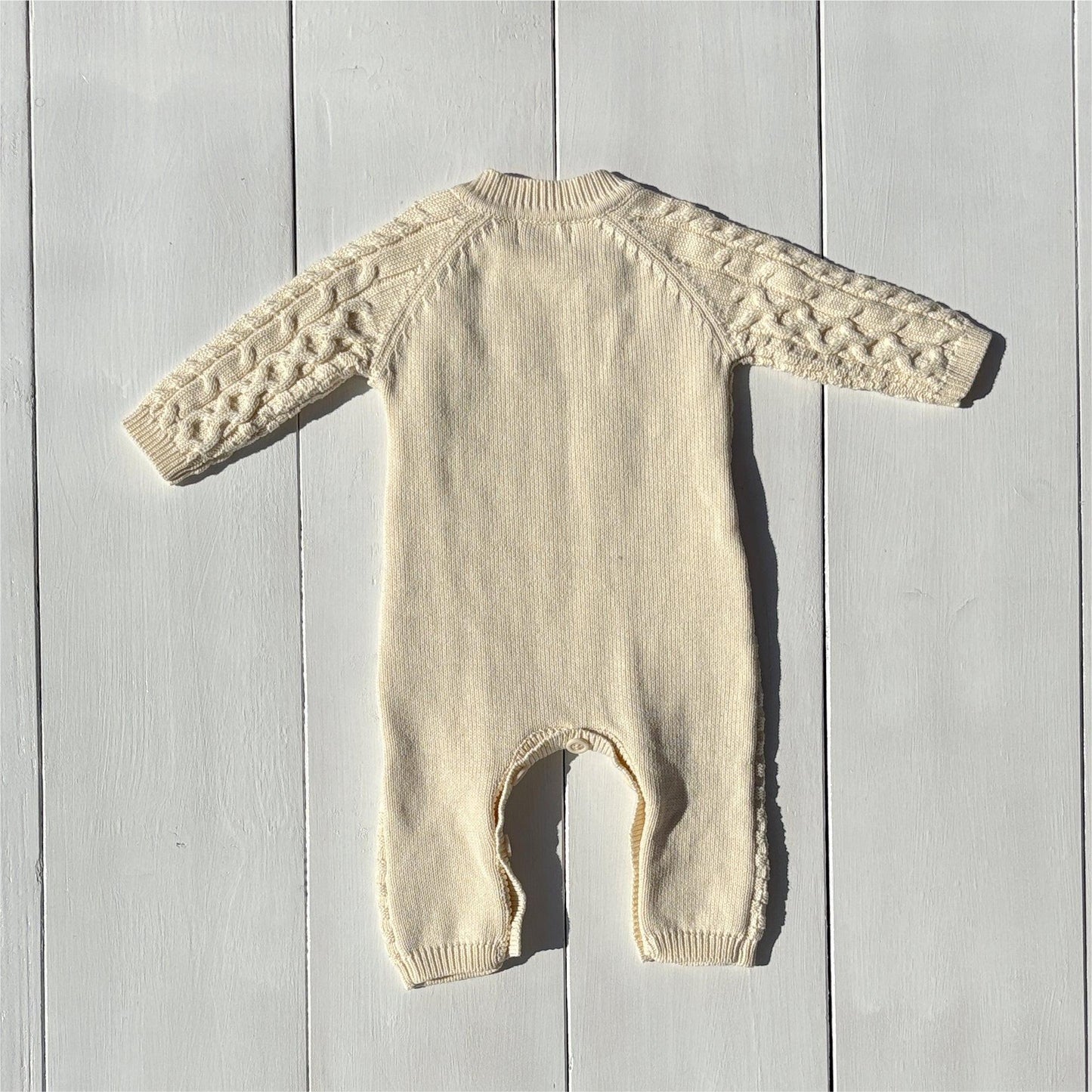 Organic knitted baby romper in cream with cable details, certified organic baby clothing by Casita Bebes.