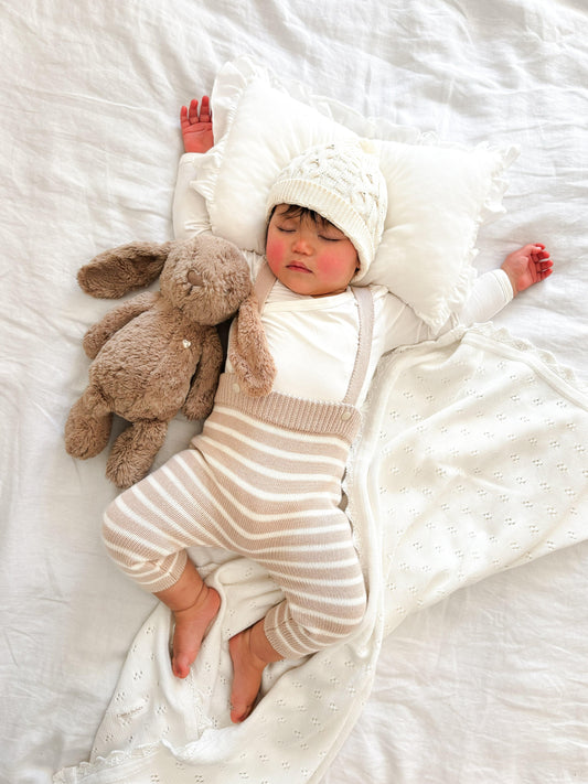 Baby wearing organic Casita Bebes knitted overalls in cream and beige stripes, certified organic baby clothing.
