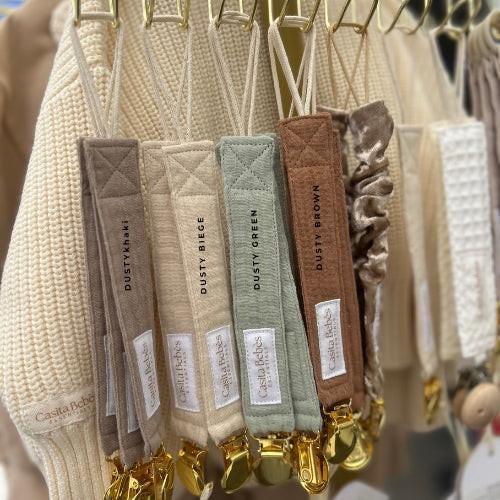 Organic baby pacifier clips in dusty beige, green, brown—soft, quilted, gold-clipped essentials for newborns