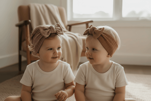 Two babies in organic cotton onesies with bow headbands, cozy indoor setting