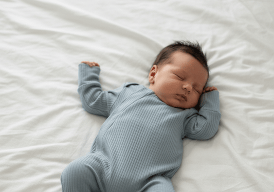 Newborn baby in a blue onesie lying on a white bed