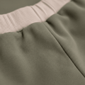 Soft olive green baby pants with pink ribbed waistband, organic cotton texture close-up