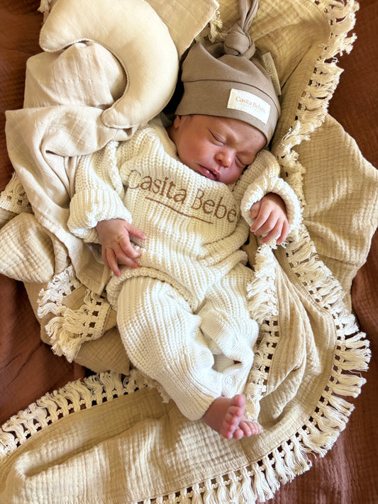 Newborn baby in a beige outfit with 'Casita Bebes' branding, wrapped in a textured blanket.