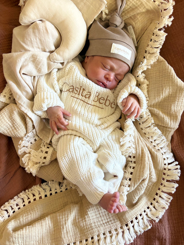 Newborn baby in a beige outfit with 'Casita Bebes' branding, wrapped in a textured blanket.