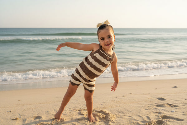 Child in a striped swim knit wear standing on a beach with ocean waves in the background