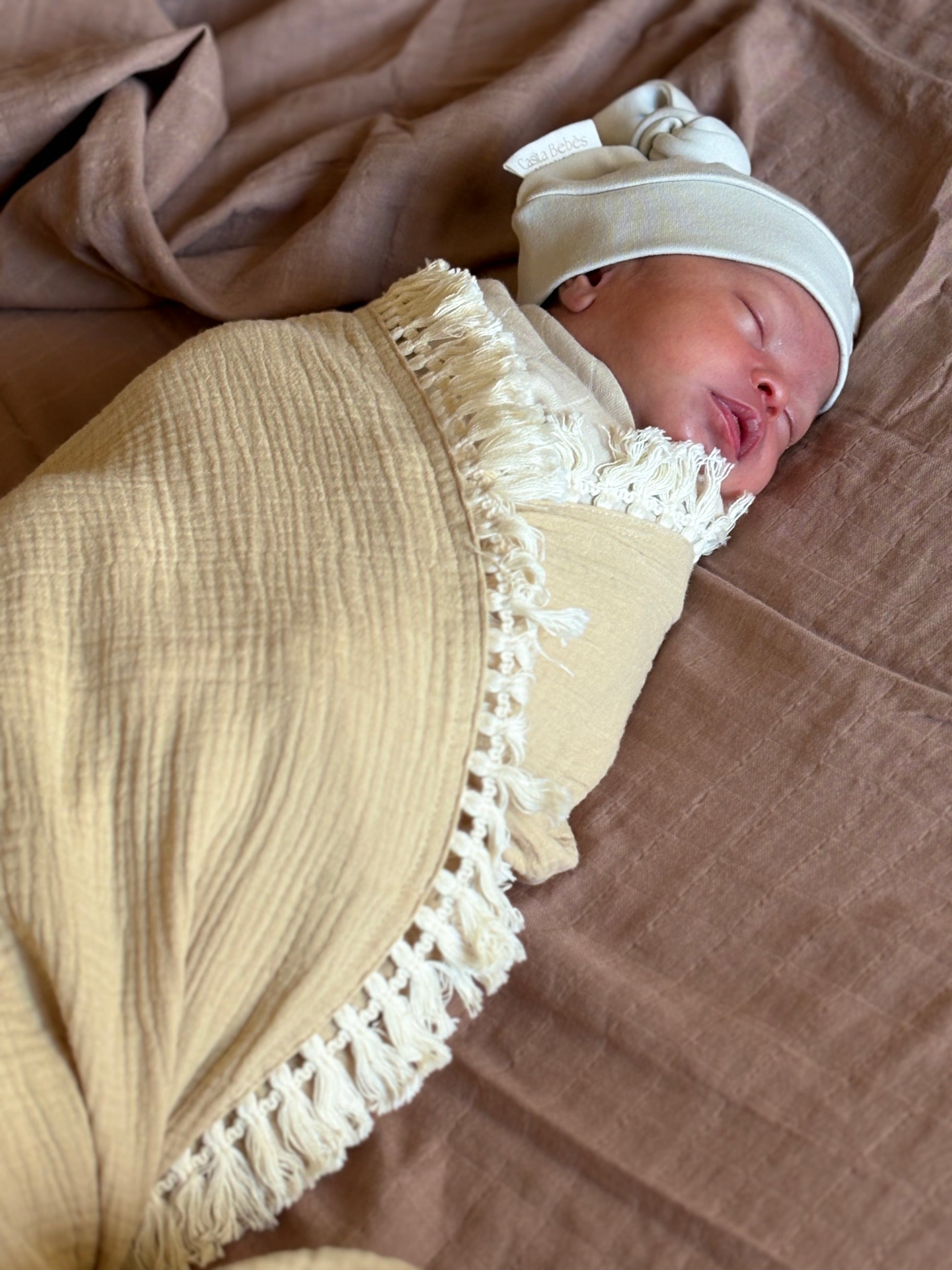 Newborn baby wrapped in Essentials Neutral Tuscan Tassel Blanket withe essentials cloudy beanie