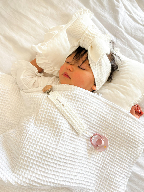 Newborn wrapped in organic Casita Bebes Essentīals waffle blanket with matching headband and mittens.