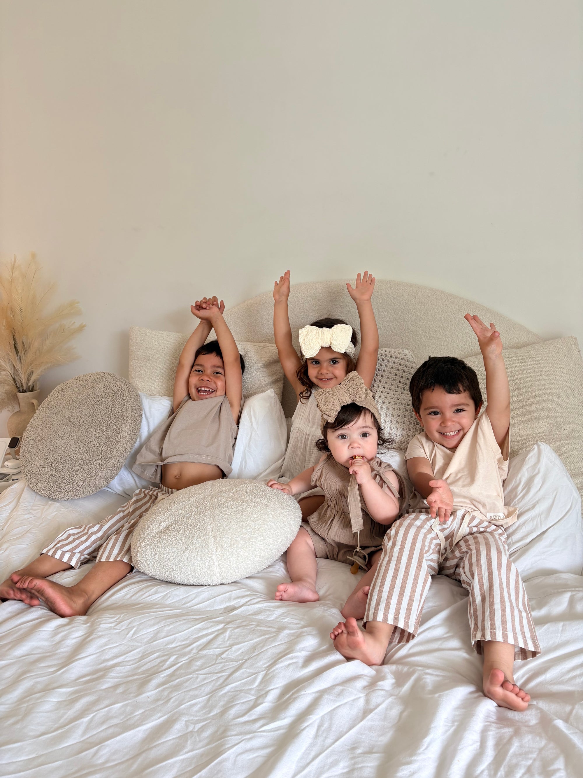Four children in Casita Bebès sitting on a bed with white bedding.