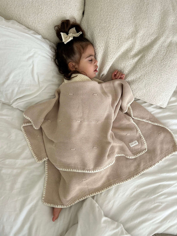Close up Child wrapped in a brown knitted blanket on a white bed