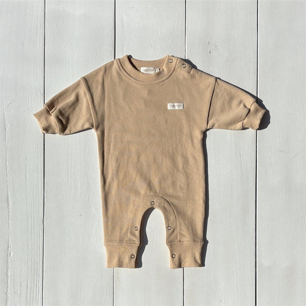 Organic baby romper in beige with snap buttons, laid on white wood background