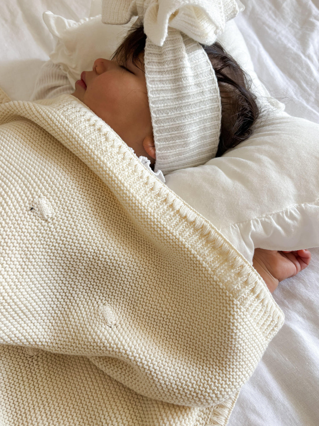 Baby sleeping in cozy organic knit blanket and matching hat, soft cream tones for gentle comfort.