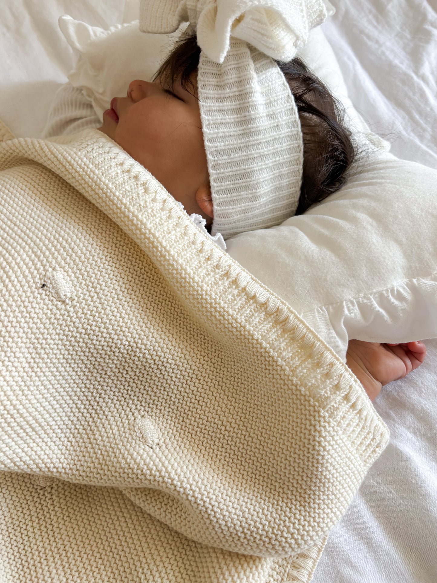 Close Up Baby wrapped in a cream knitted  blanket with a white headband, lying on a white surface.