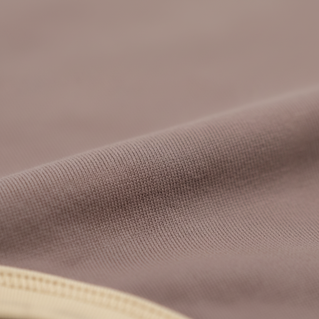 Close-up of soft mauve organic cotton fabric from Mamīta Alaina bodysuit with cream trim detailing.