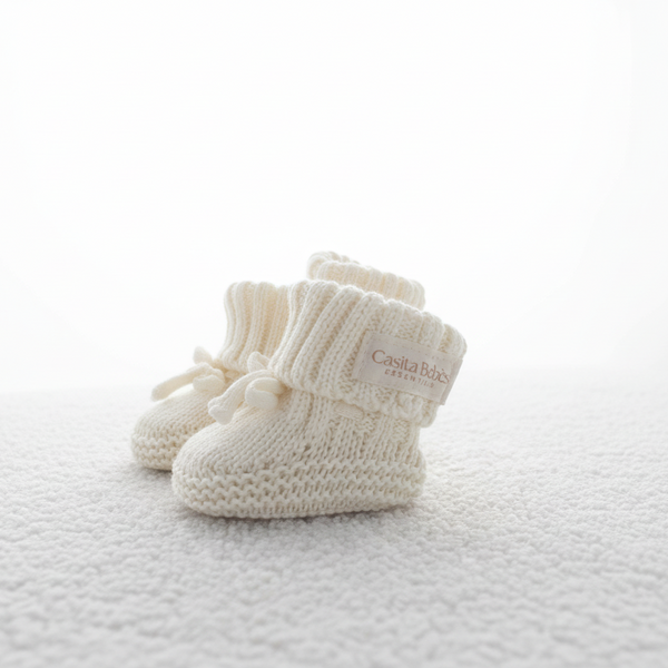 Pair of white baby booties on a textured white surface