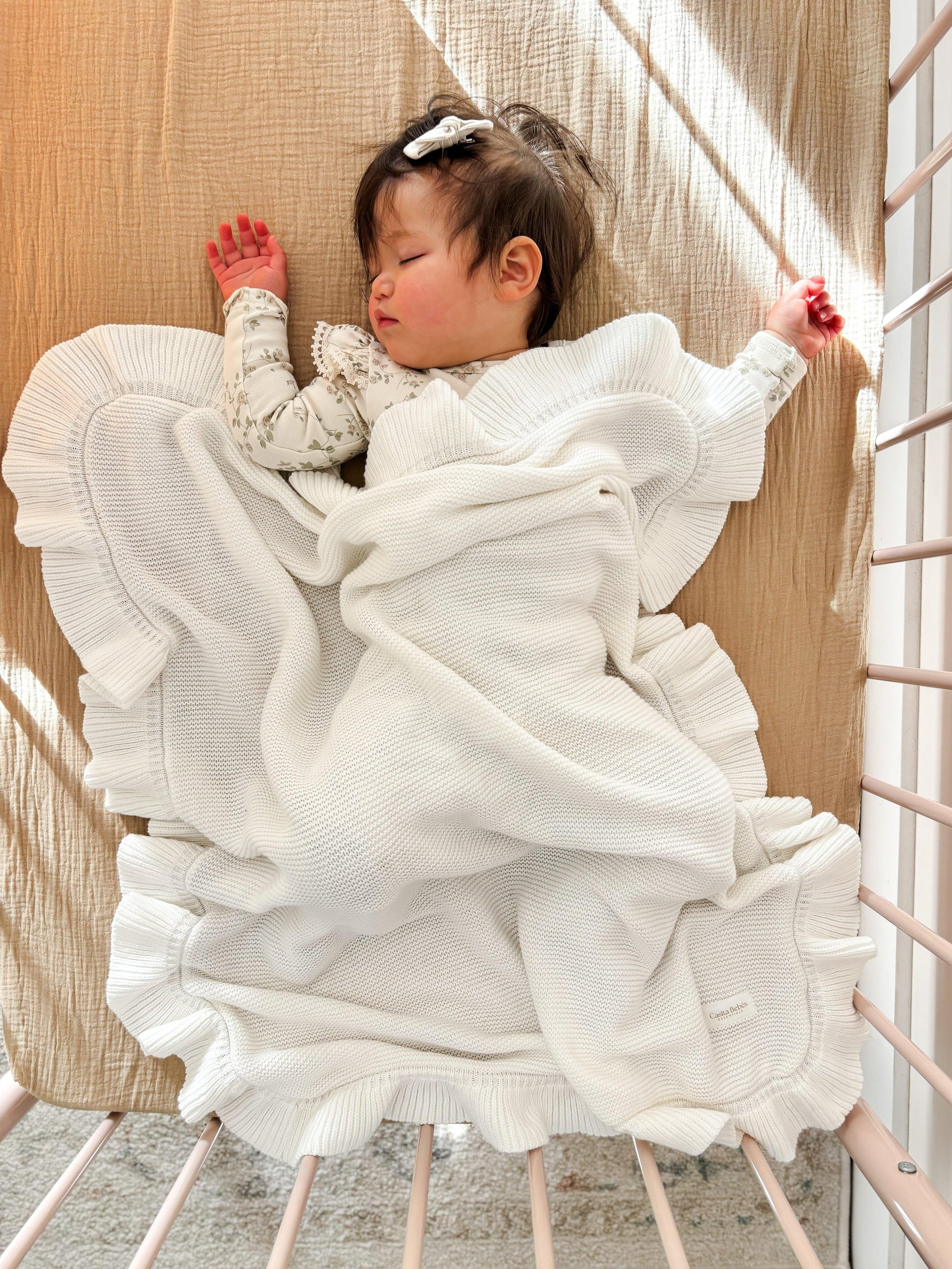 Organic soft white knitted baby blanket with ruffled edges from Casita Bebes, shown on sleeping baby.
