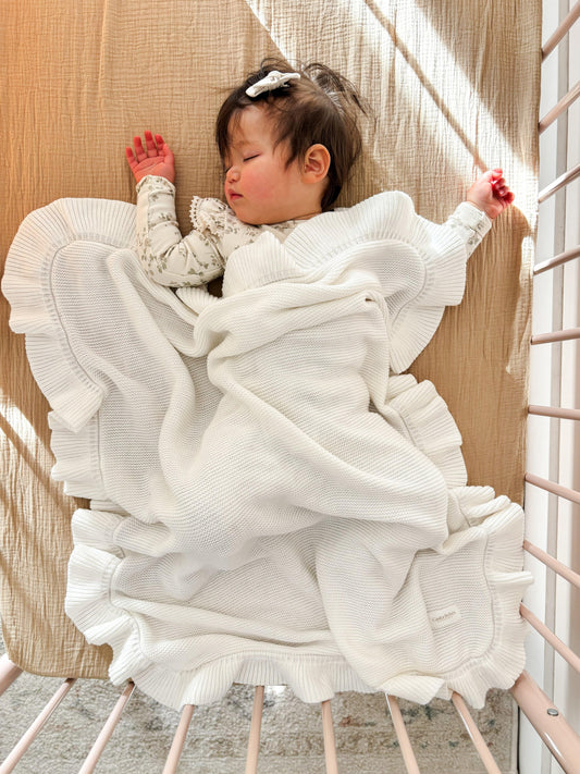 Organic soft white knitted baby blanket with ruffled edges from Casita Bebes, shown on sleeping baby.