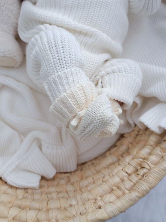 White knitted fabric  booties on a woven surface Casita Bebes brand