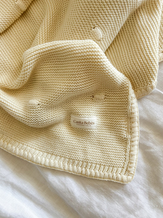 Knitted cream blanket with Casita Bebes brand label on a white background