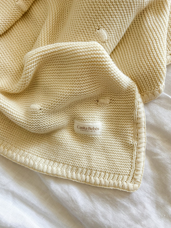 Knitted cream blanket with Casita Bebes brand label on a white background
