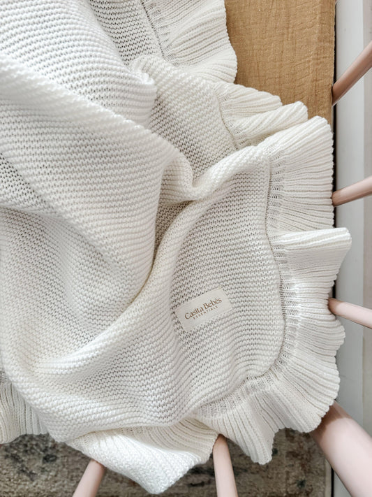 Soft white organic knitted baby blanket with ruffled edges and Casita Bebes label.