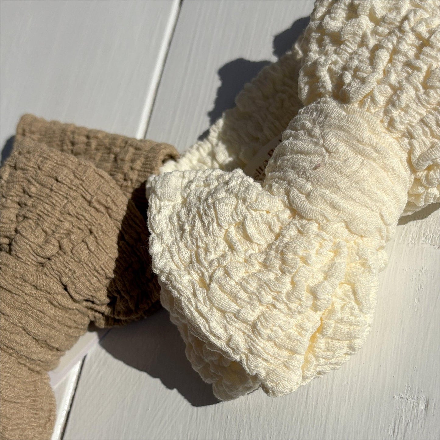 Soft organic baby blankets in cream and beige, textured for gentle comfort on white wood.