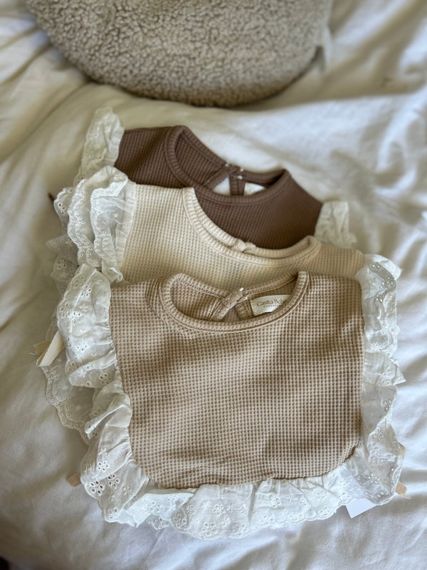 Three flat lay baby bibs with lace trim on a white surface