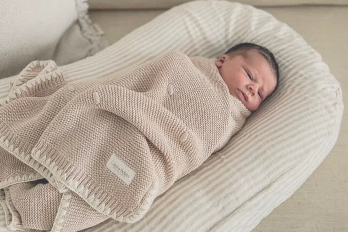 Newborn baby swaddled in a beige blanket on a textured pillow
