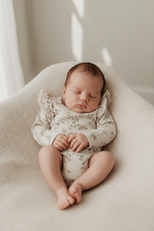 Baby in floral organic onesie sleeping on textured blanket, gentle early motherhood essentials