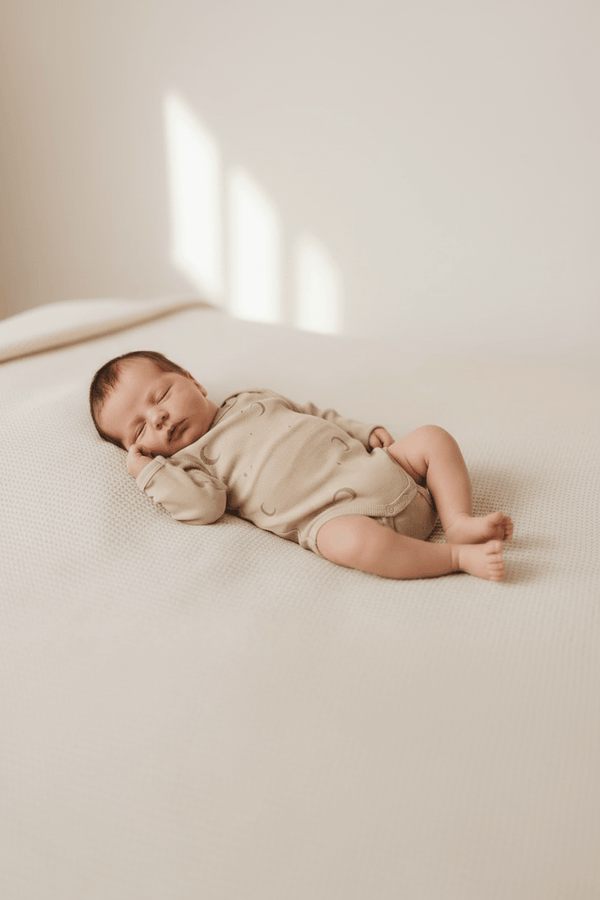 Newborn baby sleeping peacefully in organic cotton onesie with moon print, nestled on soft blanket