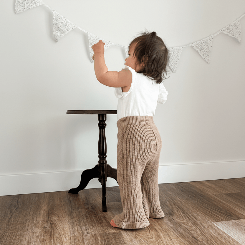 Baby in organic ribbed pants and white top reaching for lace bunting