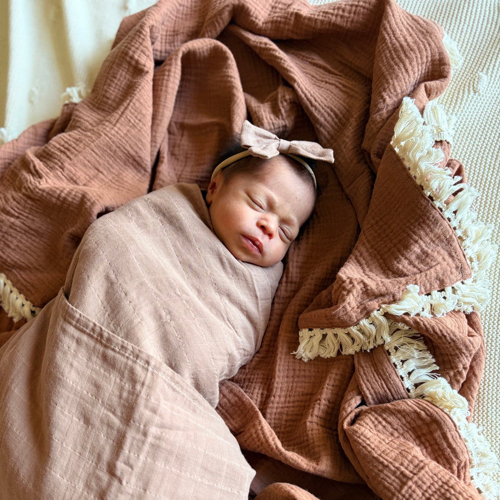 Newborn baby swaddled in a pink blanket with a bow on a textured surface