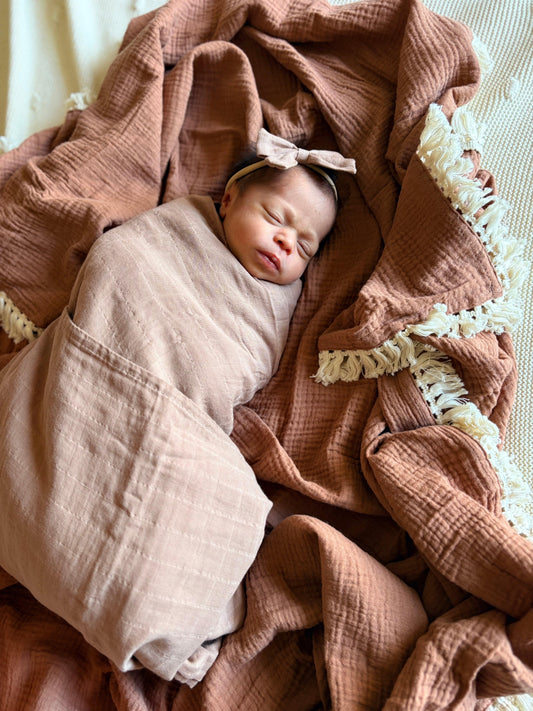 Newborn baby swaddled in a pink blanket with a bow on a textured surface