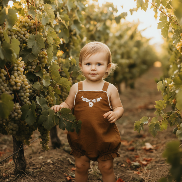 Baby girl in Mamīta Siena Pinfore standing among grapevines in a vineyard wearing brand Casita Bebes