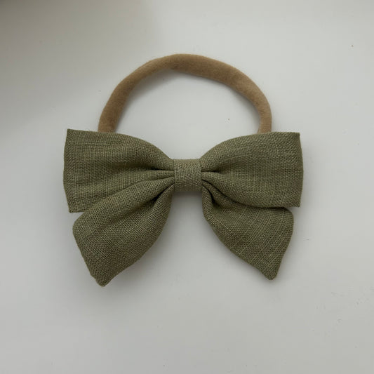 Green bow hair accessory on a beige elastic band against a white background