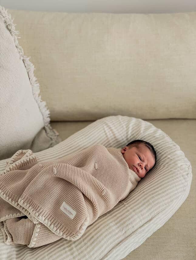 Newborn baby wrapped in organic knit blanket, resting on striped cushion, cozy and serene