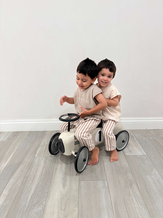 Two children playing on a small bike indoors with a plain white wall background casita bebes