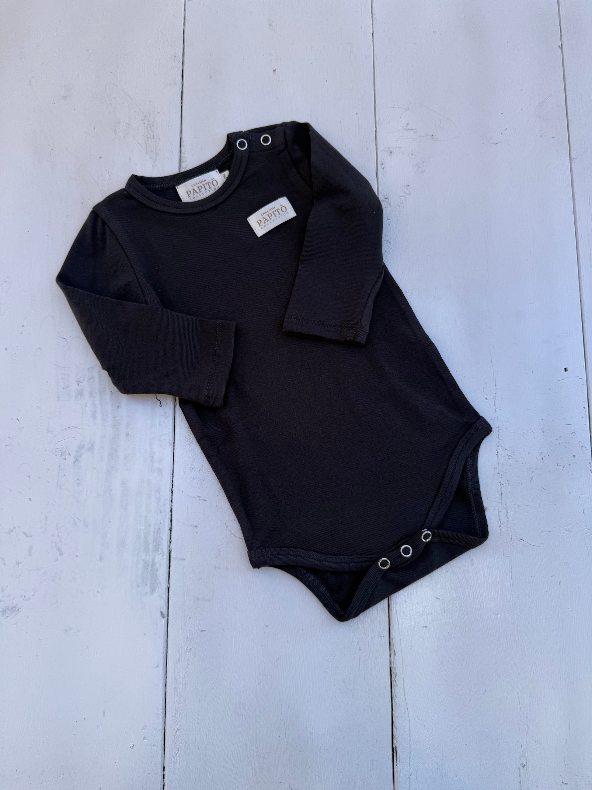 Black baby bodysuit with long sleeves on a light wooden floor Casita Bebes