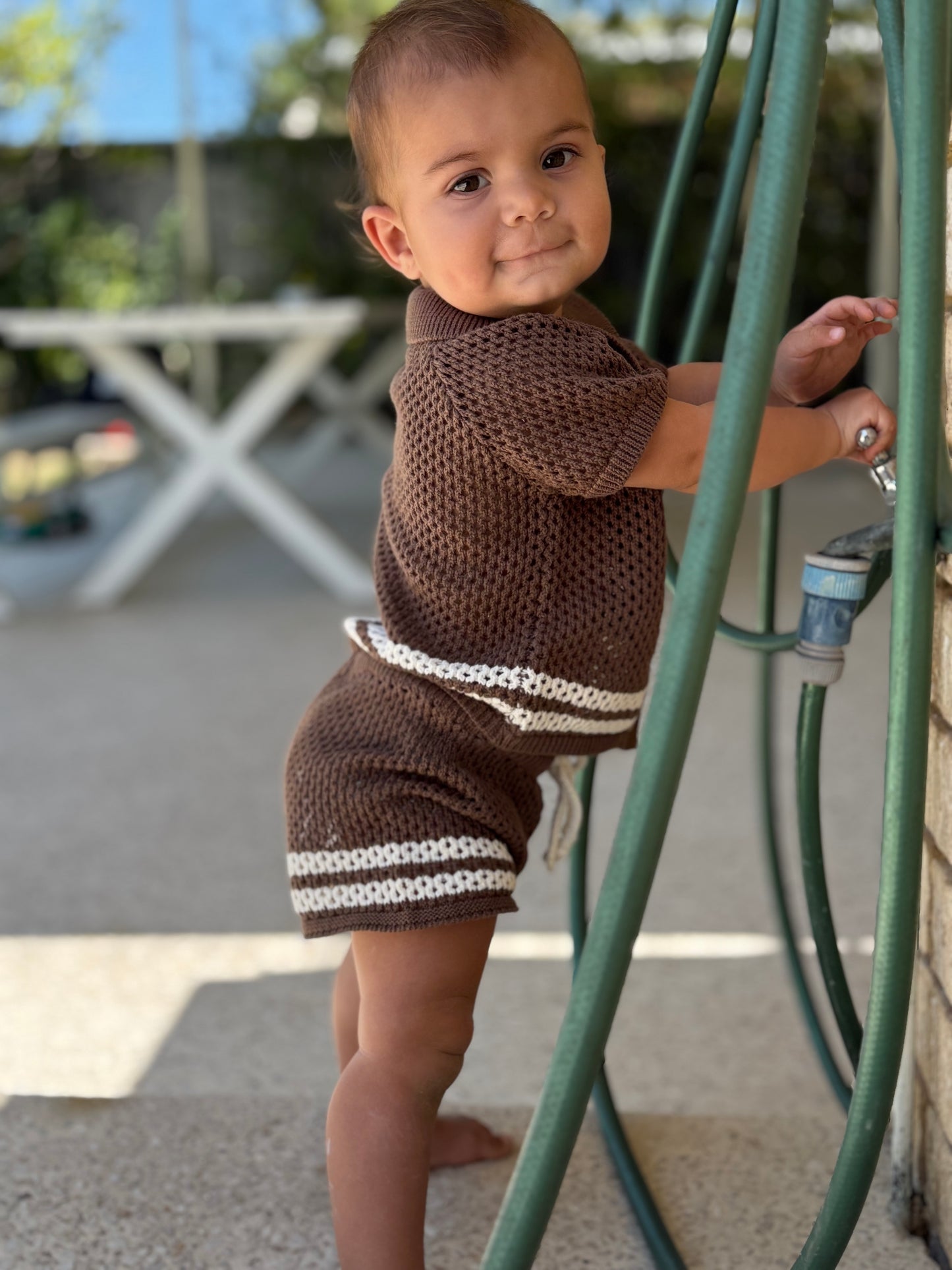 Baby wearing a brown knitted swim  cover up outfit  outdoors.