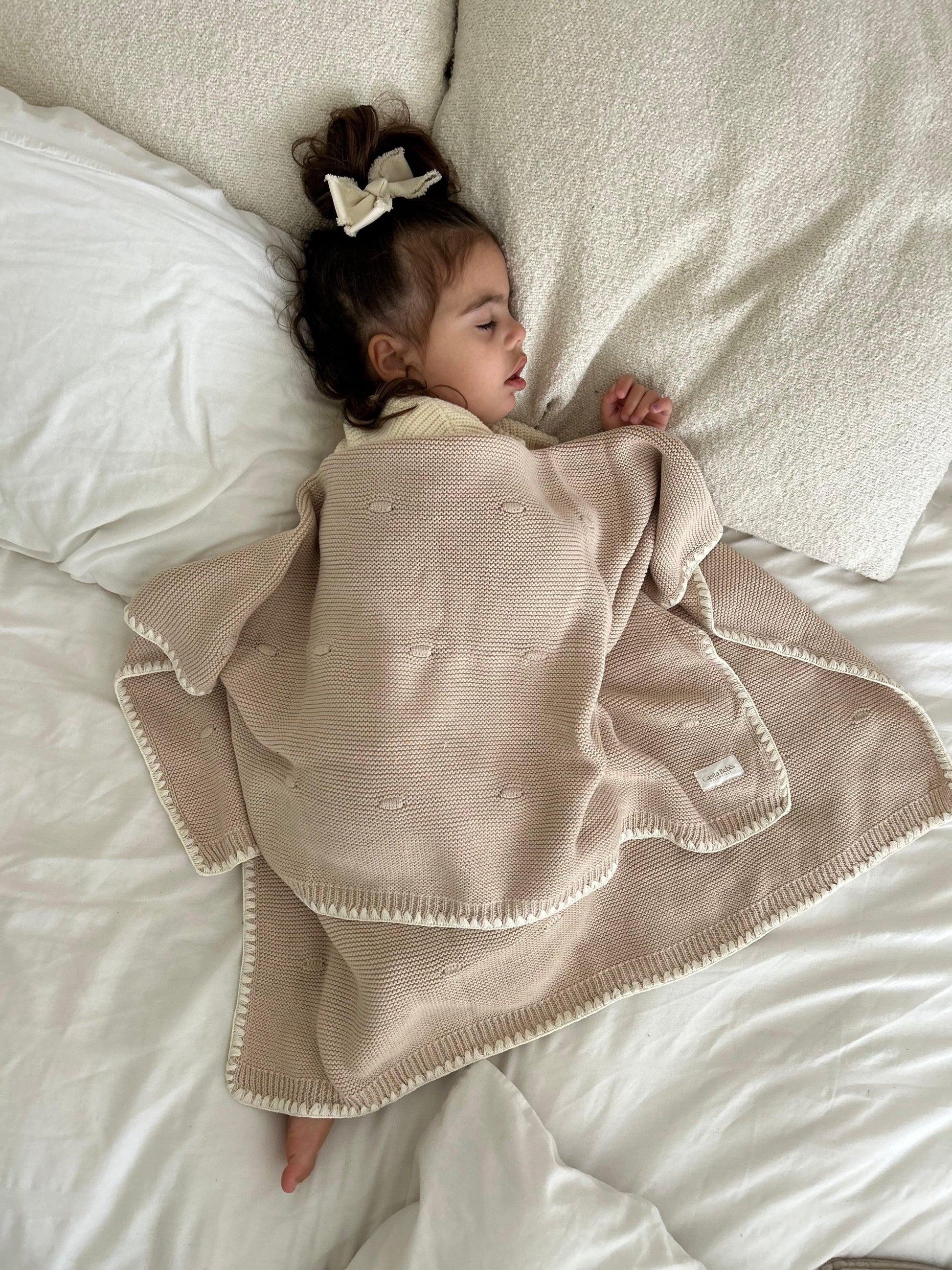 Baby wrapped in soft organic knit blanket, sleeping peacefully on cozy bed
