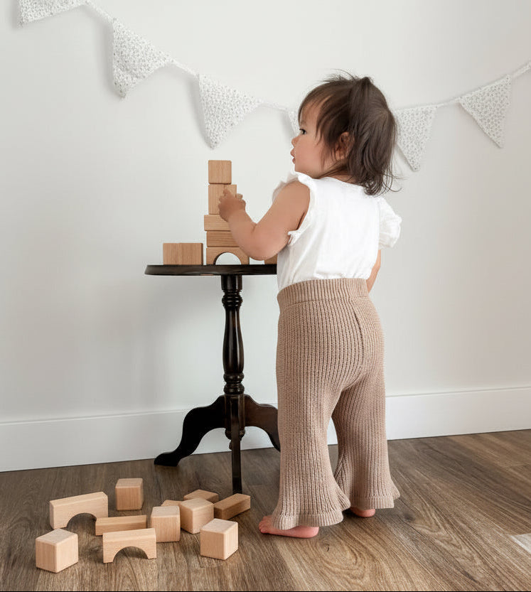 Toddler playing with wooden blocks on a wooden floor in a minimalistic room.