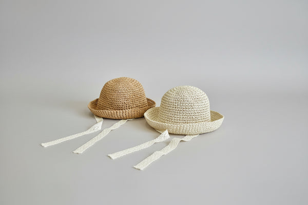 Two straw toddler hats with ribbons on a white gray background