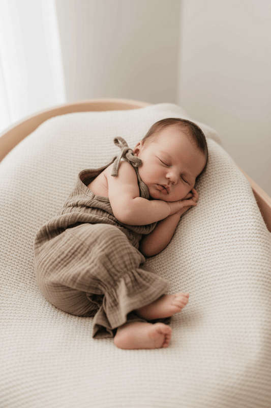 Newborn baby sleeping peacefully on a soft surface with a neutral color palette.
