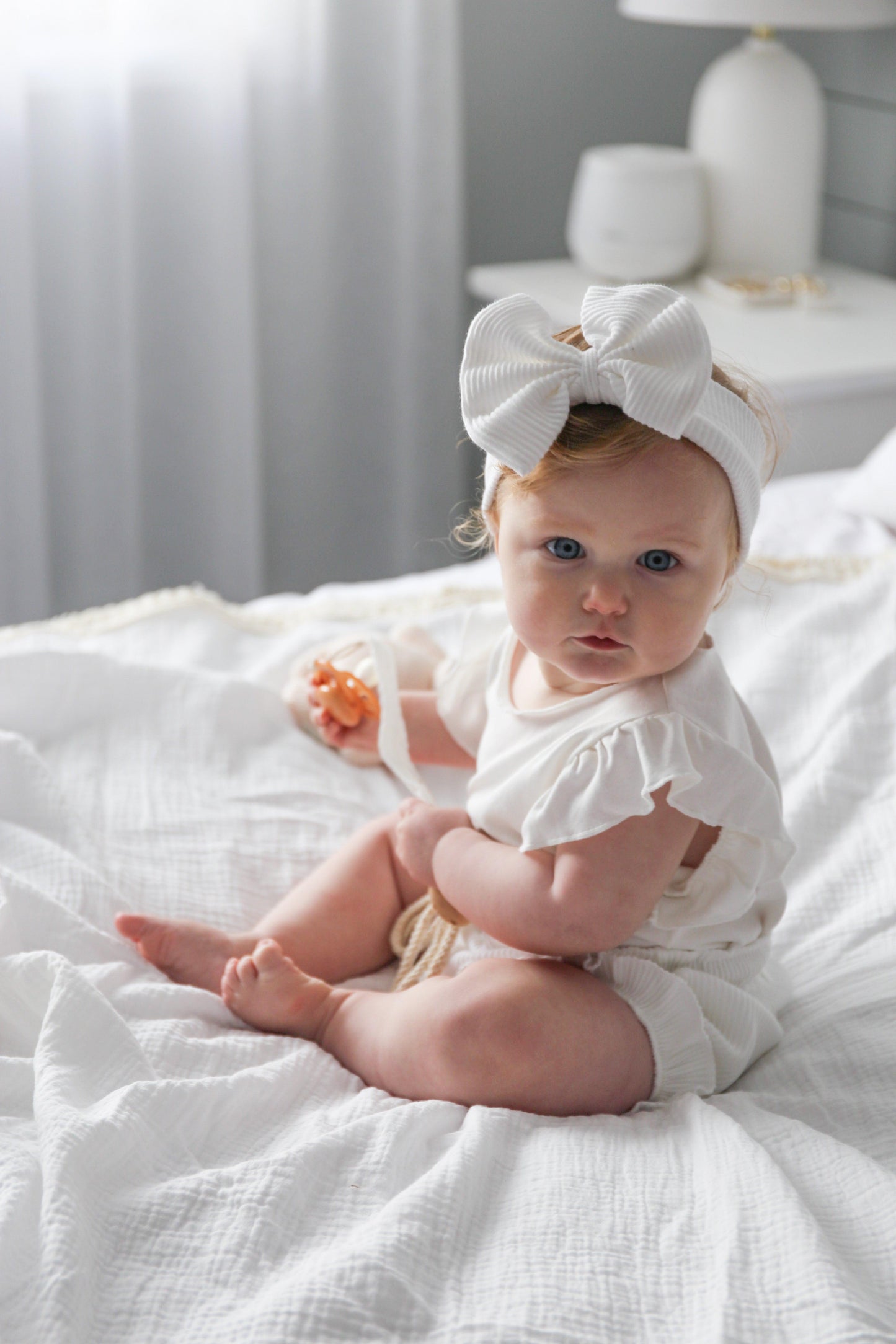 Baby wearing organic cotton ribbed bow headband and white baby clothing by Casita Bebes.