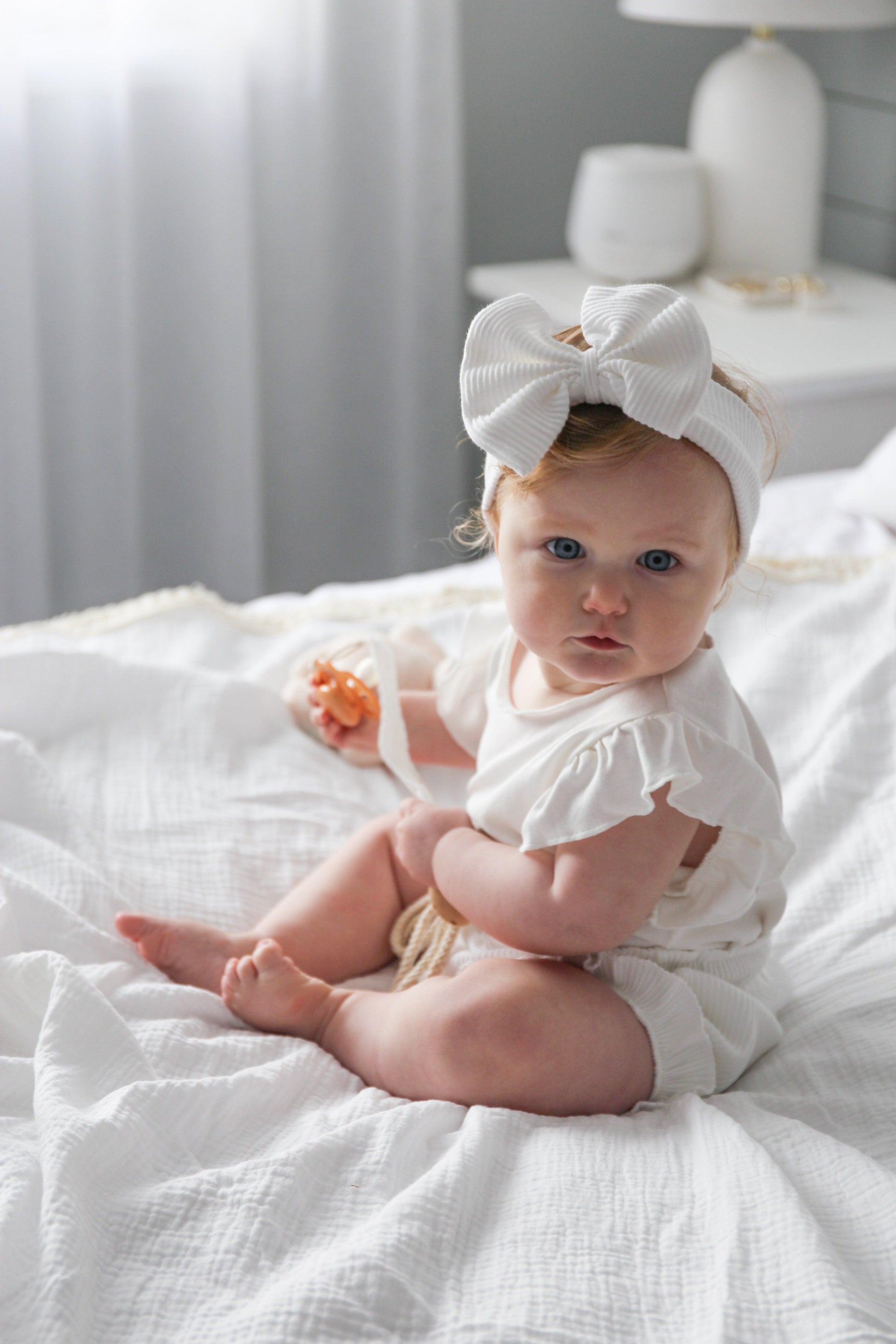 Baby wearing organic cotton ribbed bow headband and white baby clothing by Casita Bebes.