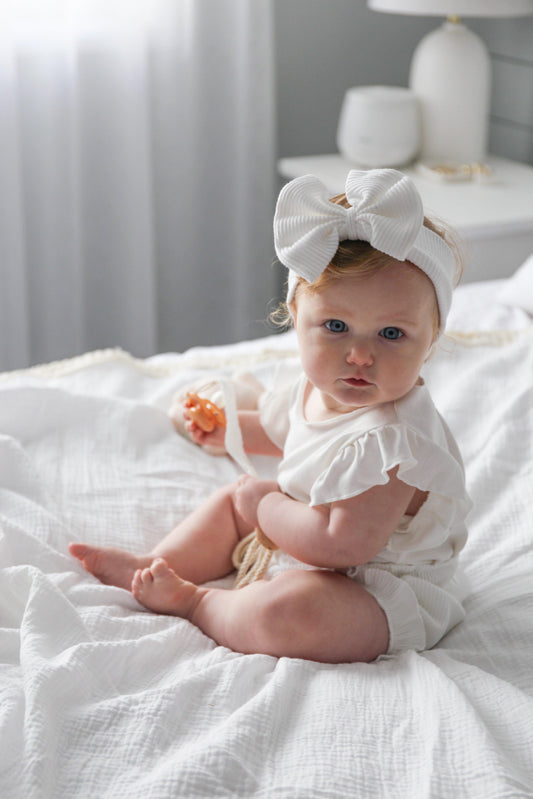 Baby wearing organic cotton ribbed bow headband and white baby clothing by Casita Bebes.